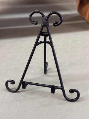 Black metal easel with decorative swirls on a neutral background