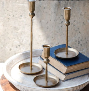 Set of three brass candle holders on a textured surface with books underneath