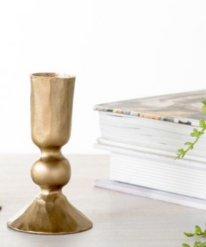 Gold candle holder on a white surface with a stack of books in the background