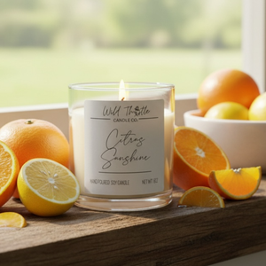 Candle labeled 'Citrus Sunshine' surrounded by oranges and lemons on a wooden surface.