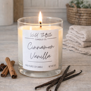 Candle labeled Cinnamon Vanilla on a wooden surface with cinnamon sticks and vanilla beans.