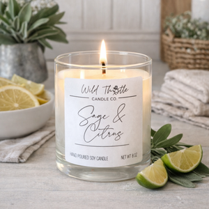 Scented candle labeled 'Sage & Citrus' from on a wooden surface with limes and sage leaves.