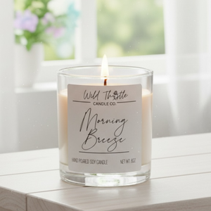Candle with a label on a wooden surface, with a blurred window and flowers in the background