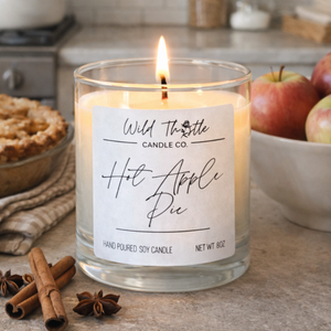 Candle labeled 'Hot Apple Pie'  on a kitchen counter with apples and cinnamon sticks.