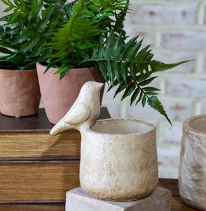 Decorative cement bird planter with green ferns in background