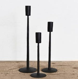 Three black candle holders of different heights on a wooden surface with a white background