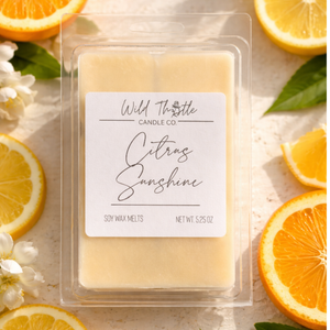 Packaged soy wax melts labeled 'Citrus Sunshine' by Wild Thistle Candle Co. surrounded by sliced oranges and white flowers.